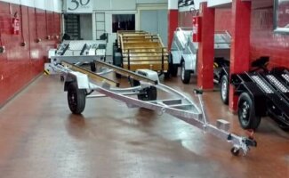 Carreta náutica galvanizada em showroom, ao lado de carretinhas para motos e carga; exemplo de carreta ideal para motos, barcos e cargas.
